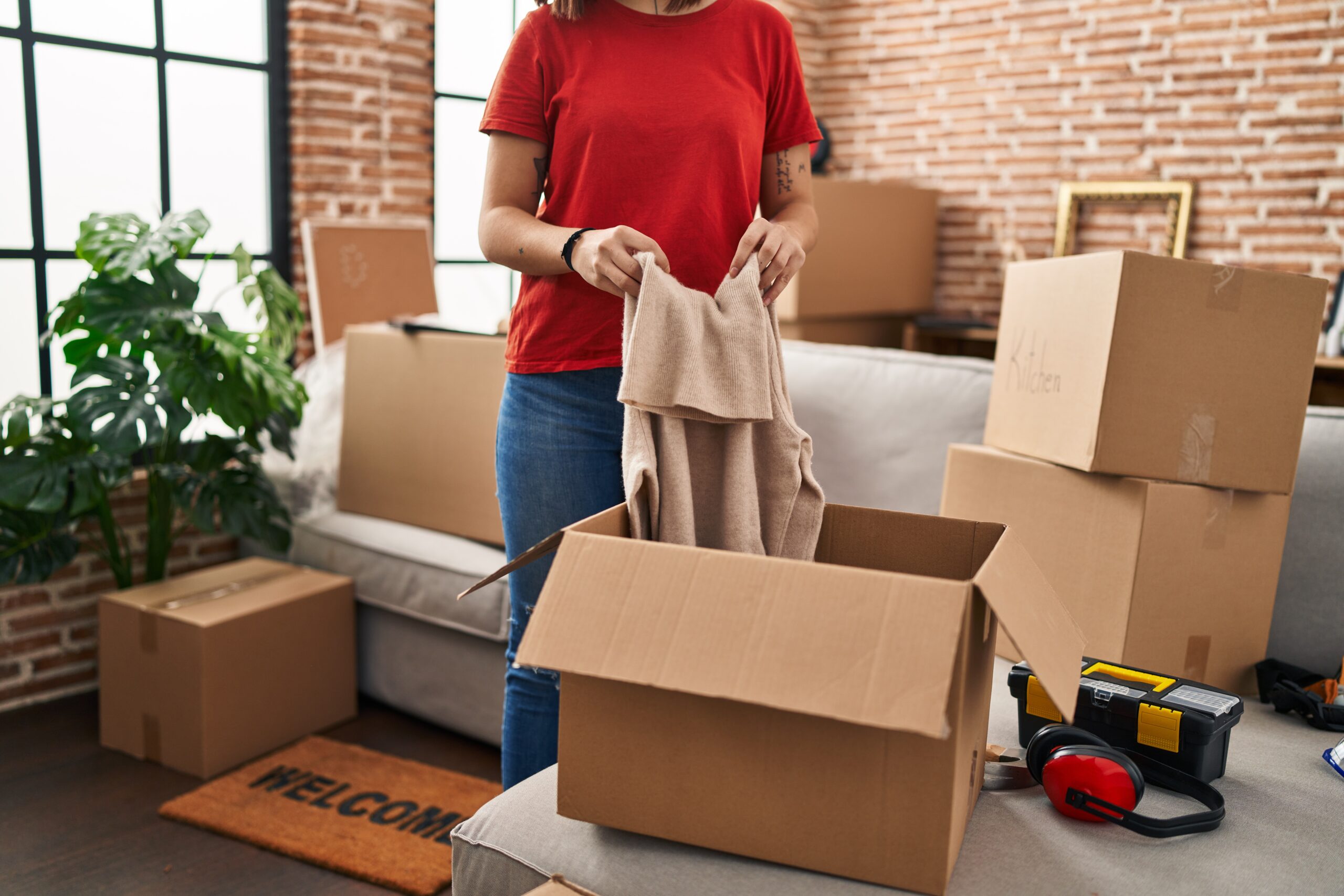 Young beautiful hispanic woman unpacking cardboard box at new home